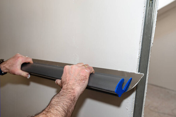 A man applies ready-made polymer plaster from a bucket using special plaster cutters.