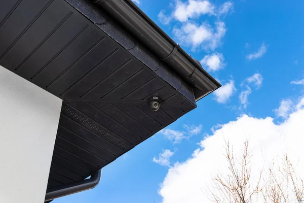 Round wireless camera mounted on the corner of the roof in the soffit, monitoring of a single-family house.