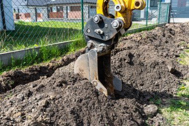 Mini kazıcı çit boyunca kanalizasyon borularına kadar bir çukur kazıyor..