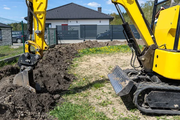 小型挖掘机沿着篱笆在花园里挖一个洞 一直通到排水管 — 图库照片