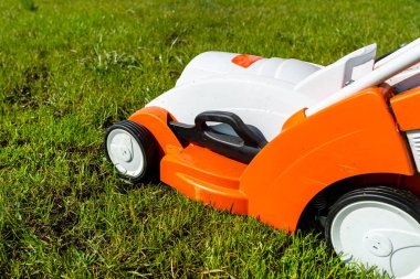 Çimlerin üzerinde duran küçük motorlu elektrikli çim biçme makinesi, turuncu renkli..