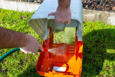 Bir adam kirli bir çim biçme sepetini suyla yıkıyor..