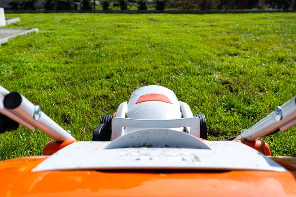 A small motorized electric mower standing on the lawn, it is orange in color.