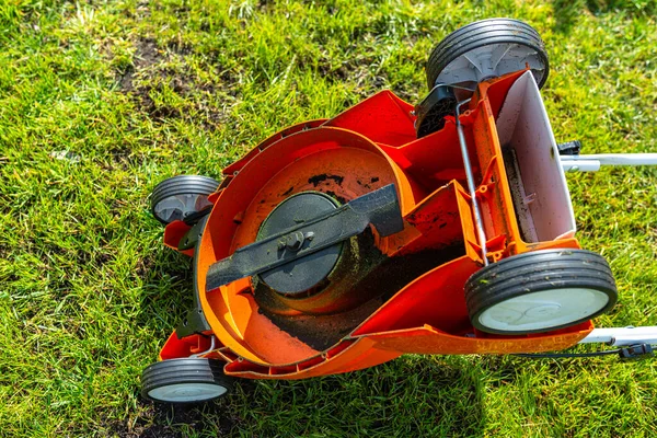A small motorized electric mower standing on the lawn, it is orange in color, visible mower blades..