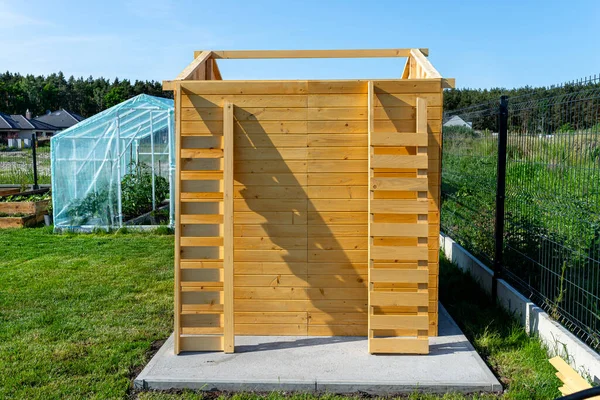 A wooden garden shed under construction standing on a concrete foundation in the garden.