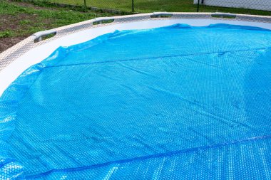 A large expansion pool with a diameter of 3.96 m, set in the yard next to the house, covered with a solar mat.