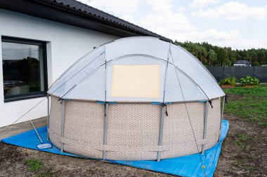 A large expansion pool with a diameter of 3.96 m, set in the yard next to the house, covered with a solar mat.
