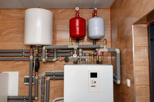 A modern air heat pump installed in the home\'s boiler room, visible plastic pipes and valves.
