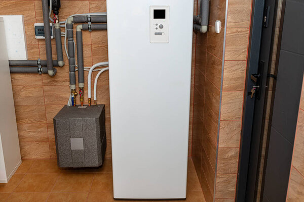 A modern air heat pump installed in the home's boiler room, visible plastic pipes and valves.