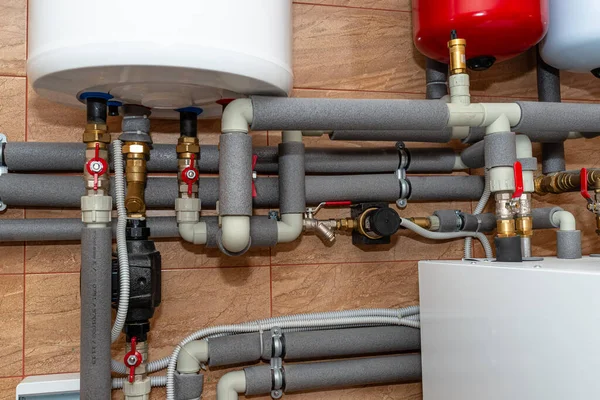 A modern air heat pump installed in the home\'s boiler room, visible plastic pipes and valves.