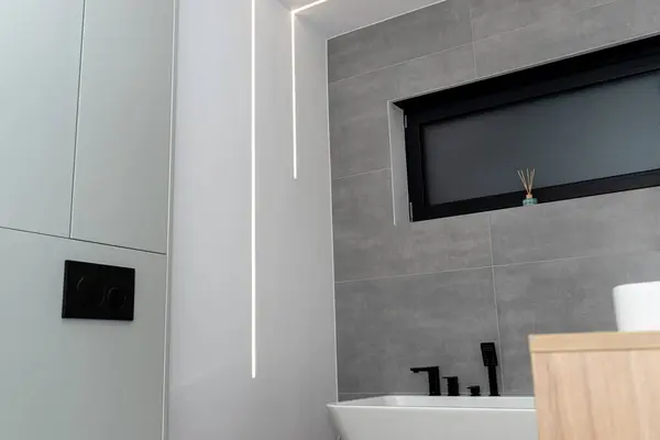LED light strips mounted in the wall in a modern bathroom, visible bathtub.
