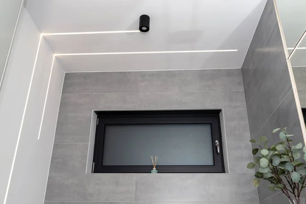 LED light strips mounted in the wall and ceiling in a modern bathroom, window visible.