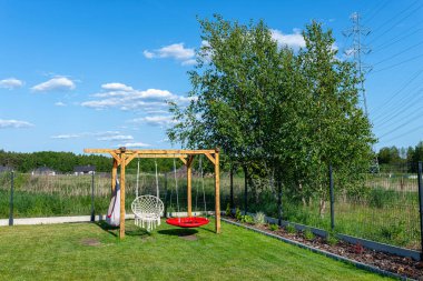 A modern cubic playground made of wooden logs and metal corners, a visible rocker and a nest.