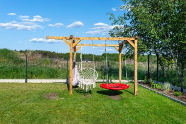 A modern cubic playground made of wooden logs and metal corners, a visible rocker and a nest.