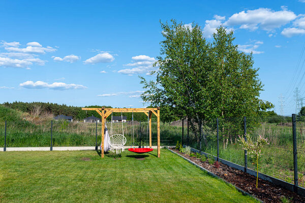 A modern cubic playground made of wooden logs and metal corners, a visible rocker and a nest.