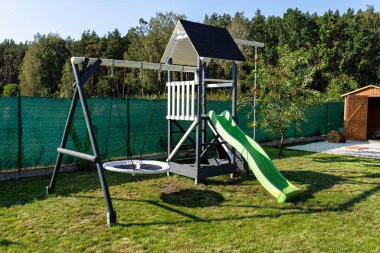 Tahtadan yapılmış, beyaz ve lacivert boyanmış, bahçede duran bir çocuk parkı..