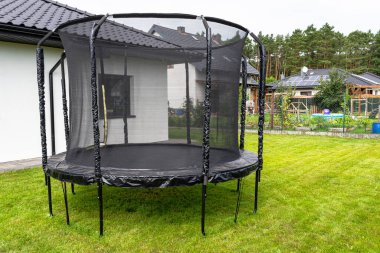 Büyük çocuklar trambolin atlarken koruyucu ağları ve kapalı fermuarları bahçede duruyorlardı..