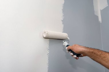 Ressam evde boya silindiri kullanarak bej renkli bir oda boyuyor..