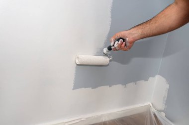 Ressam evde boya silindiri kullanarak bej renkli bir oda boyuyor..