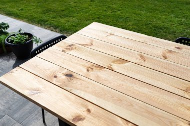 Çiğ ahşaptan yapılmış, bahçe terasında duran vernikle kaplı modern bir masa..