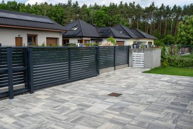 A modern panel fence in anthracite color, visible sliding gate to the garage and a garbage place in the corner.