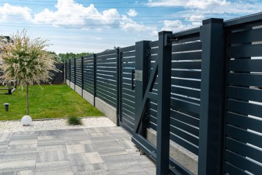 Antrasit renginde modern bir çit garaja açılan görünür bir sürgülü kapı ve posta kutusu olan bir kale..