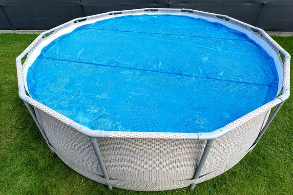 stock image Large expansion pool with a diameter of 3.96 m, located in the yard on the grass, covered with a solar mat.