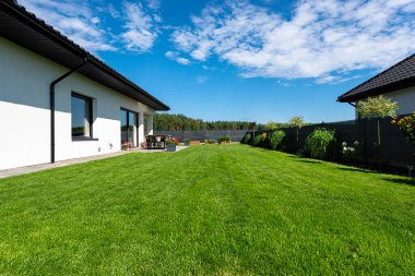 Yeşil çimenli güzel bir bahçe, görünür bir teras masası ve güzel yaz havasında bir ev, geniş açılı bir çekim..