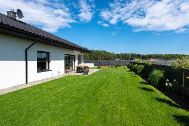 Yeşil çimenli güzel bir bahçe, görünür bir teras masası ve güzel yaz havasında bir ev, geniş açılı bir çekim..