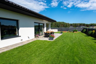 Yeşil çimenli güzel bir bahçe, görünür bir teras masası ve güzel yaz havasında bir ev, geniş açılı bir çekim..