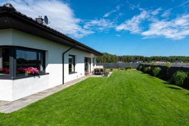 Yeşil çimenli güzel bir bahçe, görünür bir teras masası ve güzel yaz havasında bir ev, geniş açılı bir çekim..