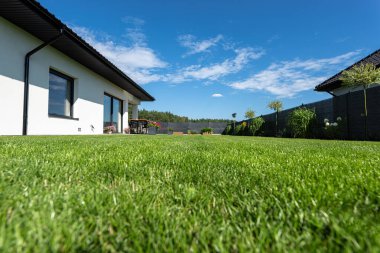 Yeşil çimenli güzel bir bahçe, görünür bir teras masası ve güzel yaz havasında bir ev, geniş açılı bir çekim..