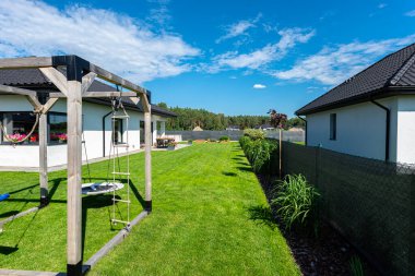 Yeşil çimenli güzel bir bahçe, görünür bir teras masası ve güzel yaz havasında bir ev, geniş açılı bir çekim..