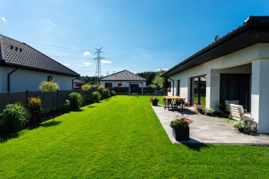 Yeşil çimenli güzel bir bahçe, görünür bir teras masası ve güzel yaz havasında bir ev, geniş açılı bir çekim..