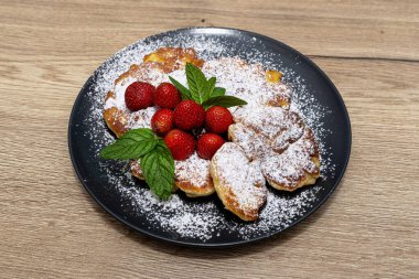 Nane yaprakları ve çileklerle süslenmiş bir tabakta duran elmalı gözlemeler..