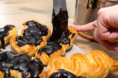 A woman spreads hot chocolate on eclairs using a silicone brush clipart