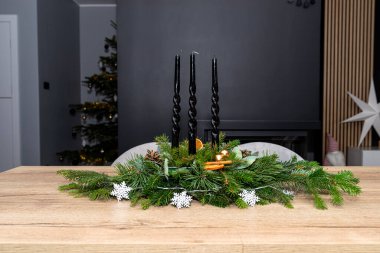 Kozalaklı dallardan yapılmış bir Noel süsü ve yemek odasındaki masanın üzerinde duran bir tahta parçası..