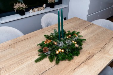 Kozalaklı dallardan yapılmış bir Noel süsü ve yemek odasındaki masanın üzerinde duran bir tahta parçası..