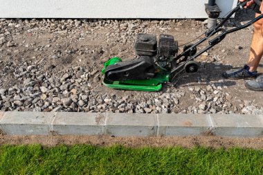 A man compacts rubble on a terrace under construction using a hand-held petrol-powered compactor. clipart