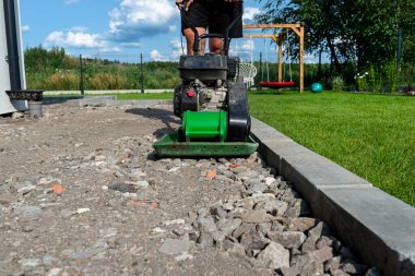 A man compacts rubble on a terrace under construction using a hand-held petrol-powered compactor. clipart