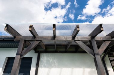 Evin arkasındaki terasın görünür kiriş bağlantıları var. Çatı polikarbonatla kaplı..