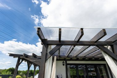 Evin arkasındaki terasın görünür kiriş bağlantıları var. Çatı polikarbonatla kaplı..