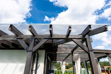 Evin arkasındaki terasın görünür kiriş bağlantıları var. Çatı polikarbonatla kaplı..