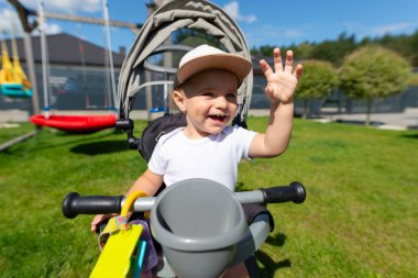 On beş aylık bir bebek evin yanındaki çimenlikte üç tekerlekli bisiklete biner..