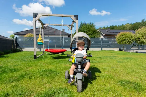 On beş aylık bir bebek evin yanındaki çimenlikte üç tekerlekli bisiklete biner..