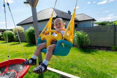 Şirin bir bebek bahçede plastik bir sallanan sandalyeye oturur..