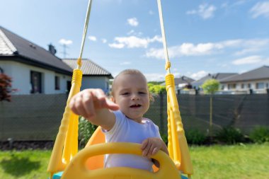 Şirin bir bebek bahçede plastik bir sallanan sandalyeye oturur..