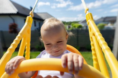 Şirin bir bebek bahçede plastik bir sallanan sandalyeye oturur..