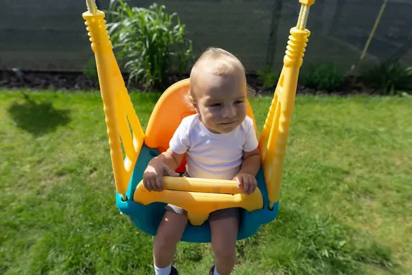 Şirin bir bebek bahçede plastik bir sallanan sandalyeye oturur..