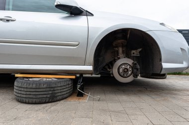 Kışlık lastiklerle değiştireceğim, evin önünde, makas krikosuyla yükseltilmiş bir araba..